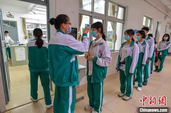 海南华侨中学学生在进入教室前有序测量体温。 骆云飞 摄 海南高三、初三开学 单人单桌上课错时就餐